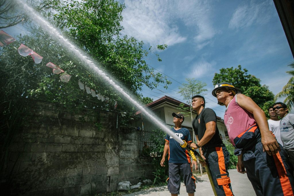 Firefighters working together to spray water during outdoor training under a clear sky.